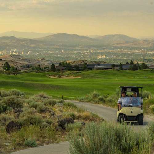 Golf cart driving up to The Club at ArrowCreek with the golf course and Reno skyline in the background