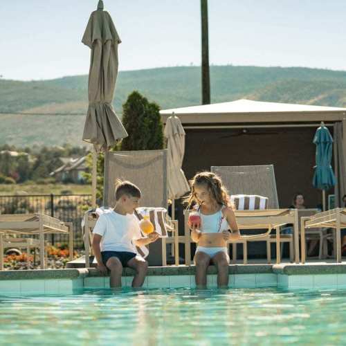 A boy and a girl sit by the pool drinking mocktails at The Club at ArrowCreek