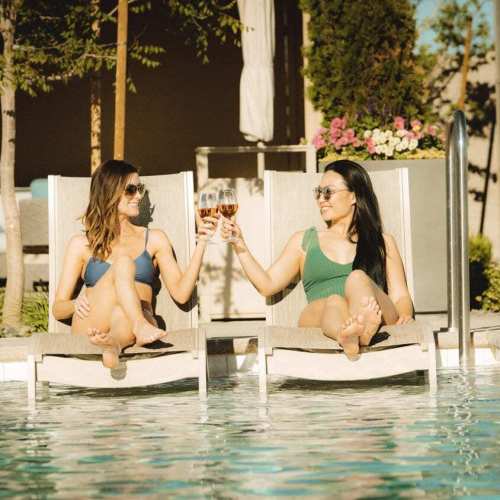 Two girlfriends cheers rose while lounging by the pool at The Club at ArrowCreek