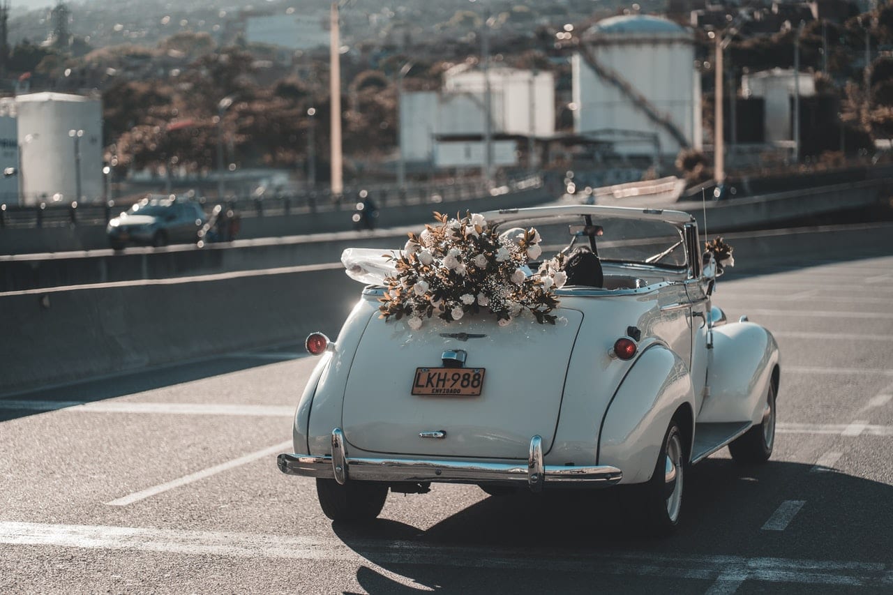 Vintage VW Bug with a wedding flower wreath drives off with the bride and groom