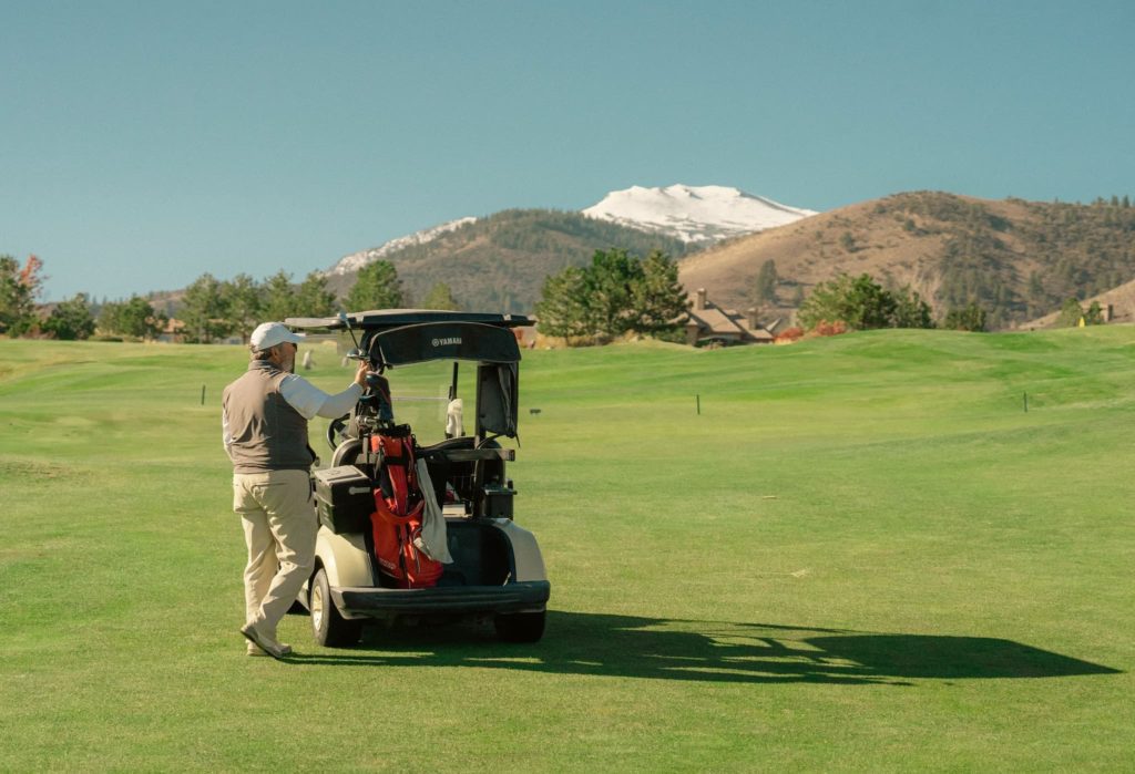 A man stands beside a golf cart on a golf course looking at the Sierra Nevada Mountains at The Club At ArrowCreek.
