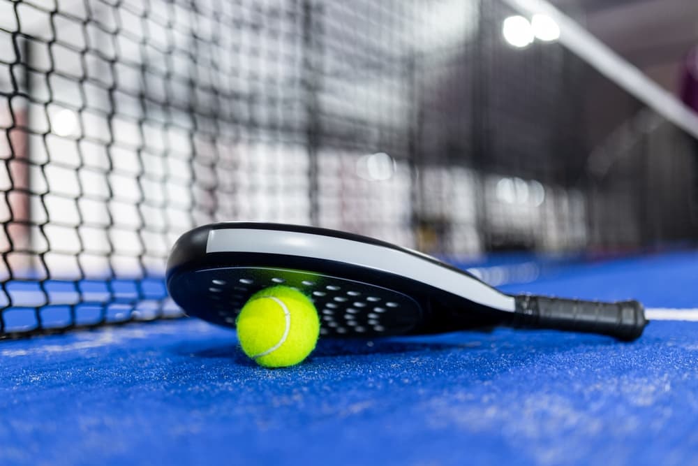 bright green pickleball with paddle on the floor of an indoor court